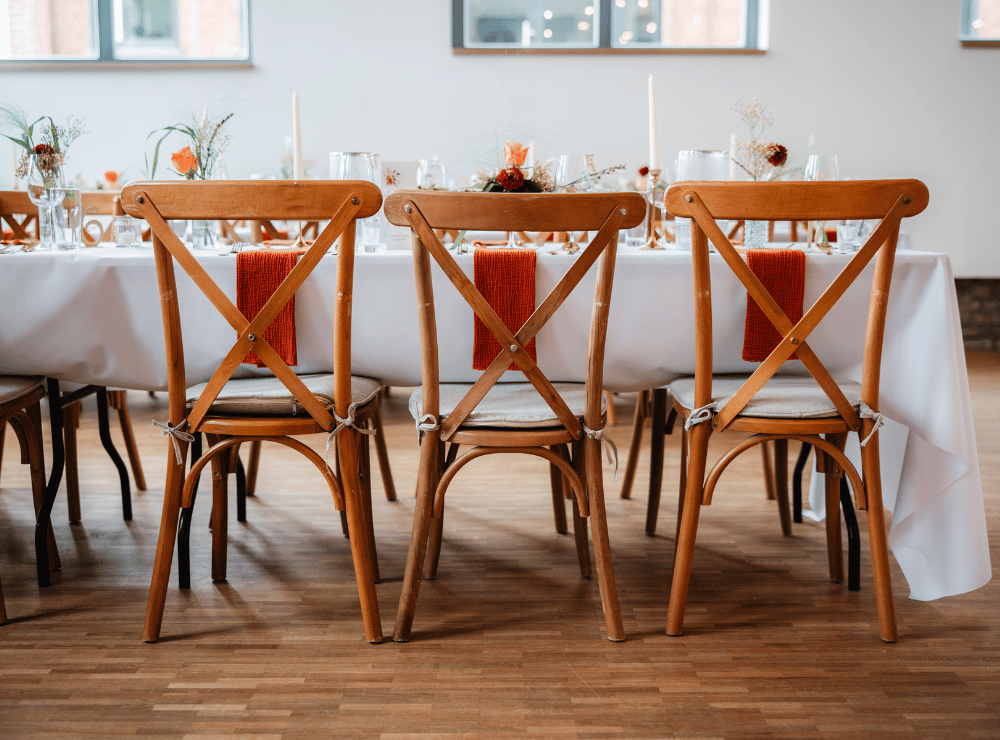 Detailansicht einer festlich gedeckten Hochzeitstafel mit weißen Tischdecken, Holzstühlen und warmen orangefarbenen Akzenten in der Alten Lehrwerkstatt Solingen